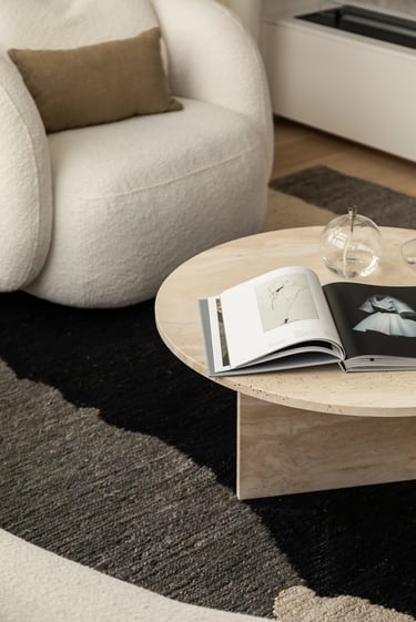 Okrągły trawertynowy stolik kawowy z albumem – detal wnętrza.