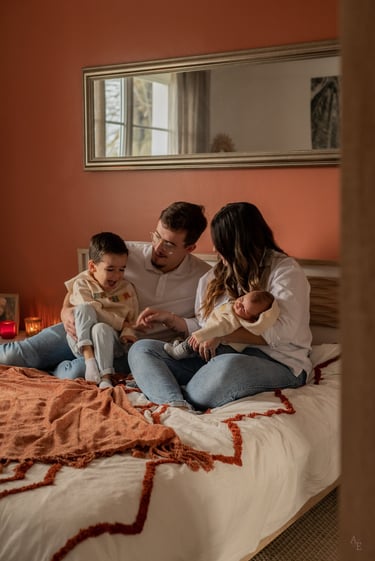 une famille de quatre personnes assis sur un lit avec un bébé dans les bras