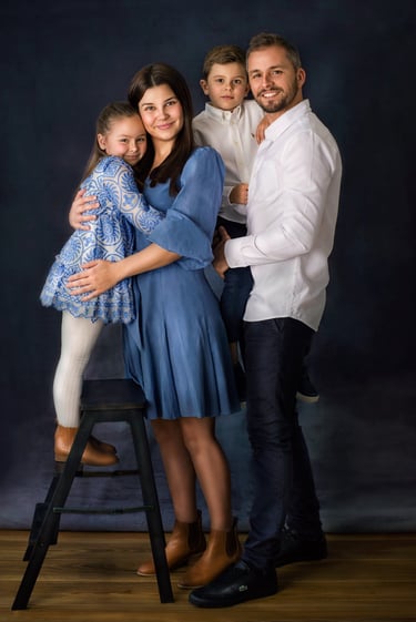 a family of four posing in a studio for a family portrait, all wearing blue and white