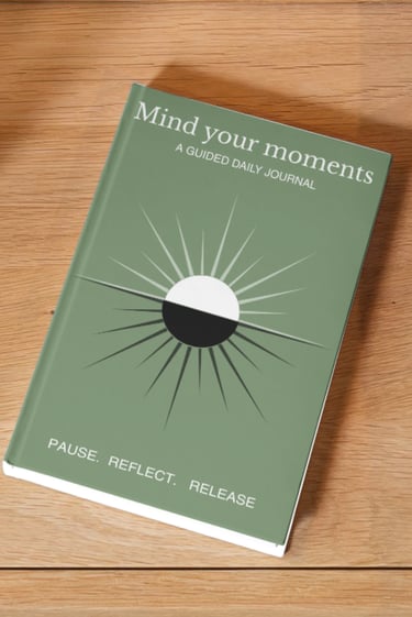 A sage green Mind Your Moments guided daily journal for mindfulness and reflection on a wooden surface.