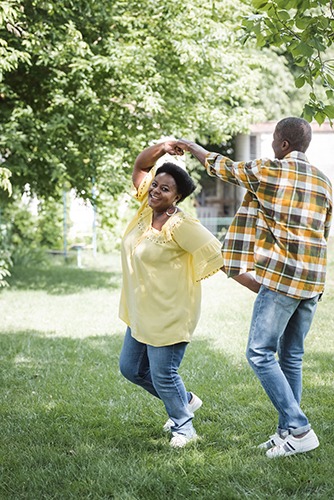 A joyful couple dancing and twirling in a sunlit green garden during summertime