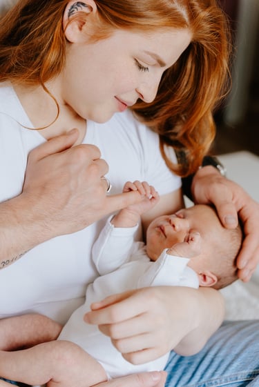 plan rapproché d'un bébé dans les bras de sa mère qui tiens un doigt de son père
