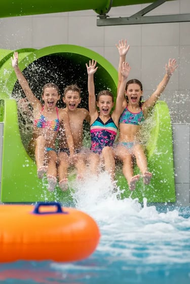 Four happy children sliding down a bright green water slide into a pool, showcasing the family-frien