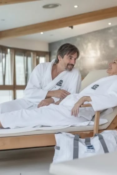 A relaxed couple wearing white spa robes, lounging and talking in a serene relaxation room at Aqua D