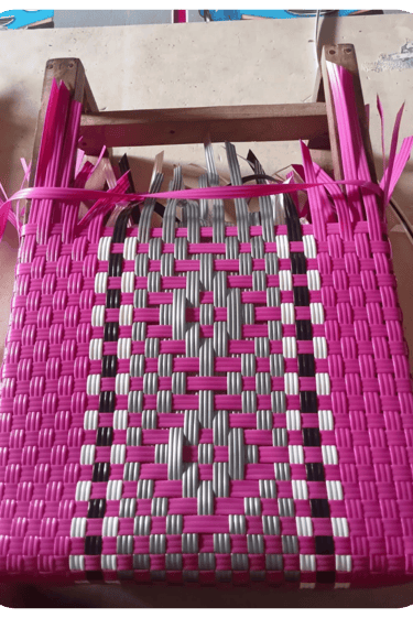 Early weaving process of a pink patterned handmade plastic woven bag at Craftvitas Indonesia.