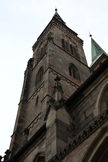 Low-angle view of the Gothic stone spires and towers of a historic cathedral against a gray sky.