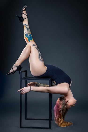 ginasta em pose artística com perna tatuada esticada e cabelos loiros jogados em fundo cinza