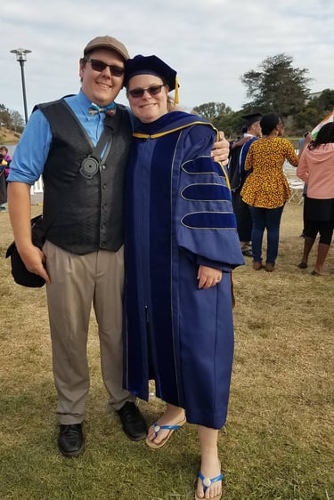 Dr. Laura Hooton, right, in Ph.D. graduation robes with husband at outdoor graduation, Santa Barbara