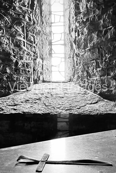 Black and white photo of a small stone cross on an altar inside a medieval castle window.