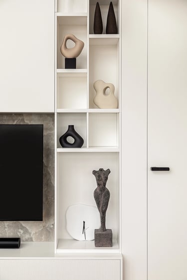 Biały regał z nowoczesnymi rzeźbami w minimalistycznym salonie.