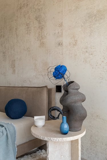 Detale sypialni: rzeźbiarski wazon i kamienny stolik nocny na tle ozdobnej ściany z tynku.