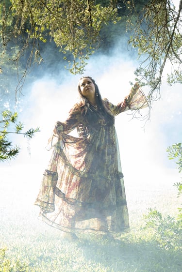 A woman in a flowing bohemian maxi dress stands in a misty, ethereal forest setting with natural sunlight.