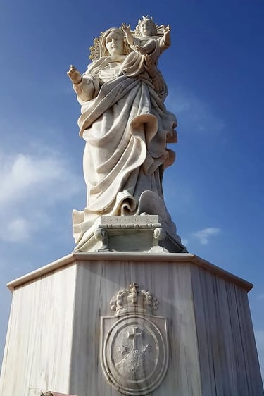 White marble statue of Virgin Mary holding Child Jesus against a blue sky background.