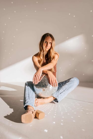 A photo of a young woman sitting in a studio, modeling with a disco ball