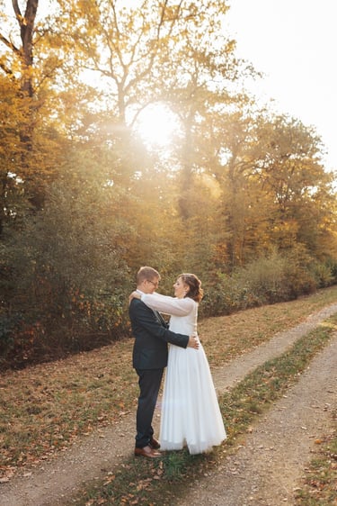 Les mariés se regardent tendrement au milieu des bois, baignés par la lumière dorée du soleil.