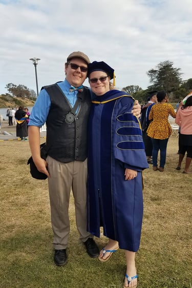 Dr. Laura Hooton, right, in Ph.D. graduation robes with husband at outdoor graduation, Santa Barbara