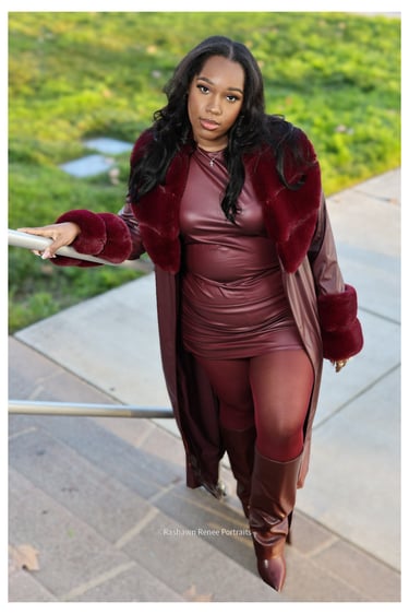 A stylish woman posing in a burgundy leather dress and faux fur coat on outdoor stairs.