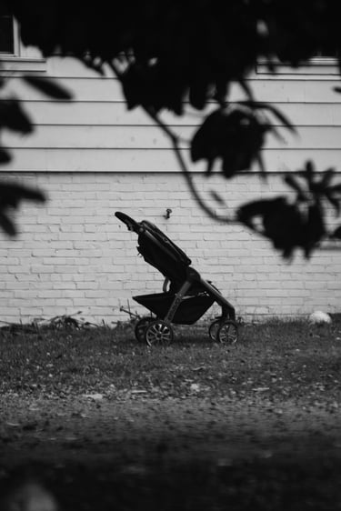 Black and white photo of an empty baby stroller parked on a lawn in front of a white brick house.