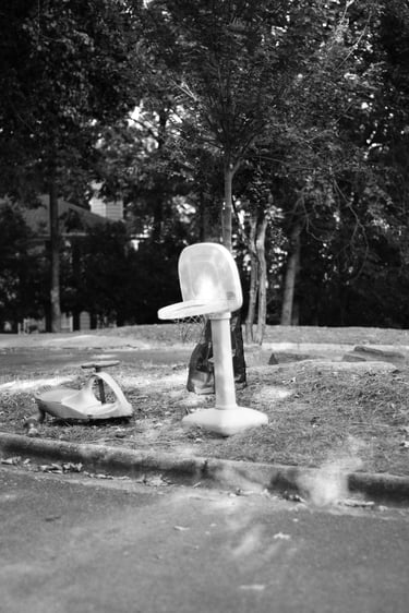 Black and white photo of a plastic toy basketball hoop and scooter on a suburban cul-de-sac.