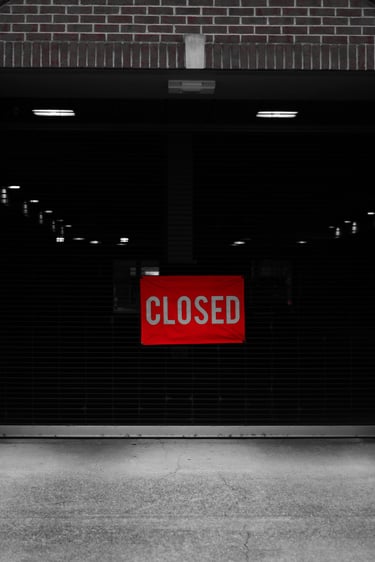 A red closed sign hangs on a dark parking garage gate entrance between two brick pillars.