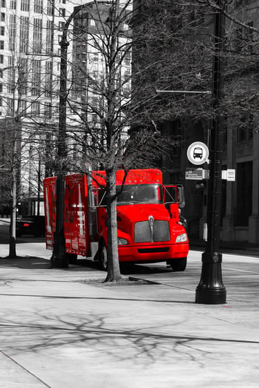 A vibrant red truck parked on a black and white city street with urban skyscrapers and bare trees.