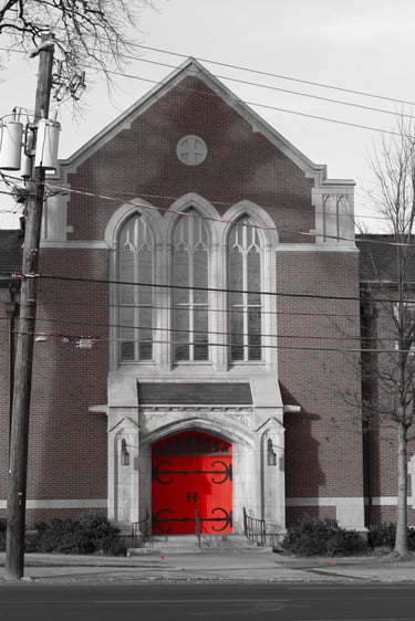 A historic brick church building with a striking bright red front door and arched gothic windows.