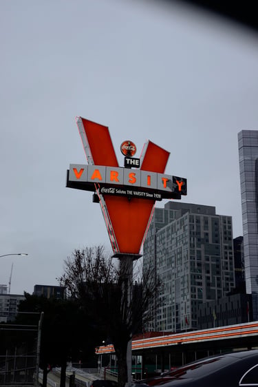 The iconic neon Varsity restaurant sign in downtown Atlanta with city buildings in the background.