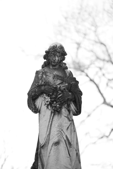A weathered stone angel cemetery statue holding flowers in a black and white portrait.