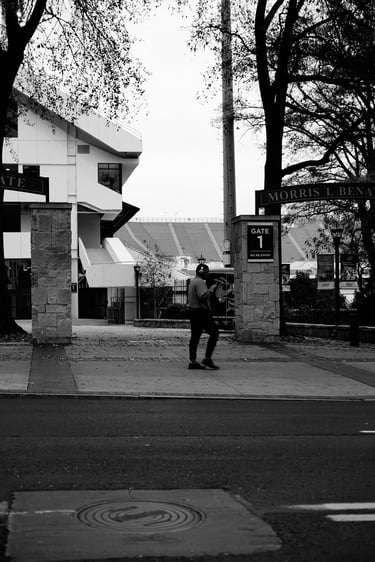 Black and white photo of a man walking past Gate 1 of the Morris L. Benatar stadium entrance.