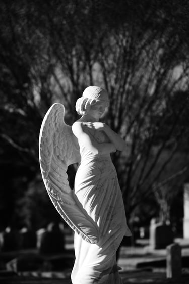 Black and white photo of a serene marble angel statue in a peaceful cemetery setting.