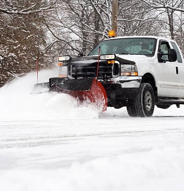 White pickup truck with a red snow plow clearing a snowy road in winter.