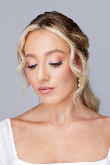 Bride with blonde hair styled softly back, soft glam wedding makeup, glowing skin, long lashes, and natural pink lipstick.