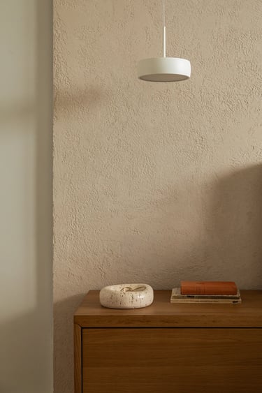 Drewniana szafka nocna, kamienna misa i biała lampa na tle beżowej ściany.