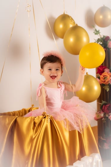 a little girl in a pink dress and a gold balloon