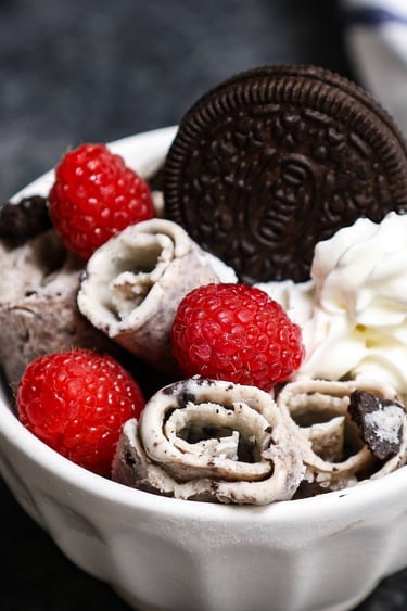 Cookies and cream rolled ice cream topped with fresh raspberries, whipped cream, and an Oreo cookie.