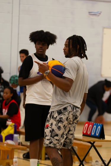 Basketball coach holding a ball and instructing a young player during an indoor sports training session.