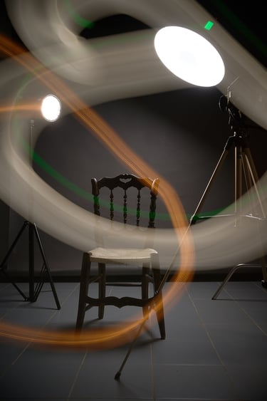 A wooden chair in a dark studio with abstract light painting trails and photography studio lights.