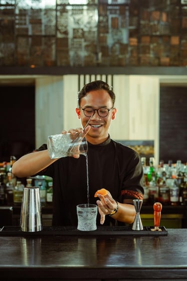 A smiling bartender pouring a clear cocktail into a crystal glass at a luxury bar.