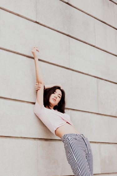 portrait de femme adossée contre un mur en pierre le bras en l'air couleur douces