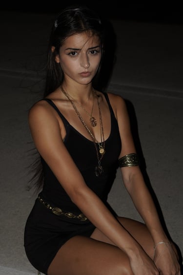 A young woman wearing a black mini dress and gold statement jewelry for a night aesthetic look.
