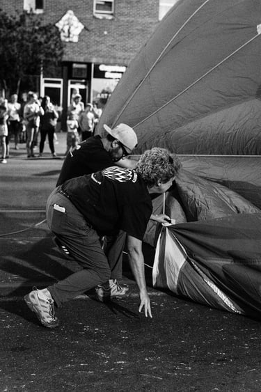 A black and white photo of people preparing a hot air balloon for inflation at an outdoor festival.