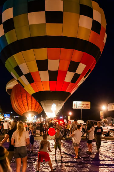 Crowd watching colorful hot air balloons glowing at night during a festival glow event.