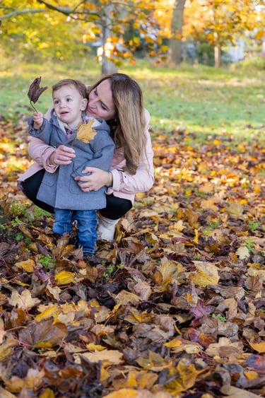 a woman and her baby looking at a leave in a park