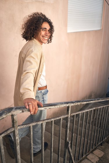 A man with long curly hair smiling at the camera on the stairs of Notre-Dame de la Garde
