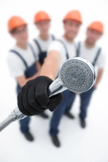 Close-up of gloved hand holding shower head with construction workers blurred in background