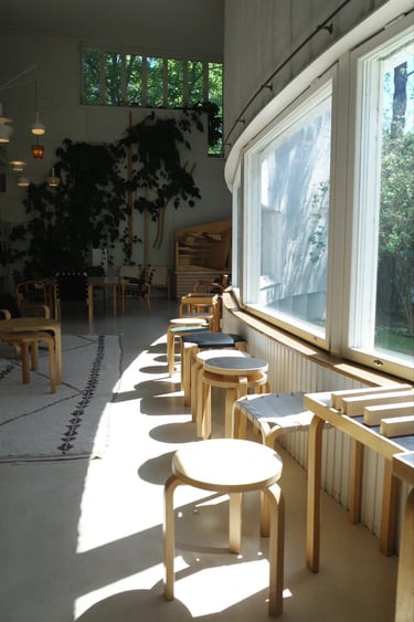 Alvar Aalto Studio room with wooden stools, soft sunlight and large windows overlooking nature