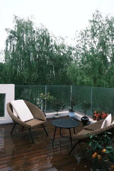Small outdoor seating area with wicker chairs, a round table, wooden decking and greenery in a moder