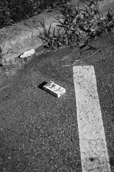 Black and white photo of a discarded Marlboro cigarette pack on asphalt next to a white road line.