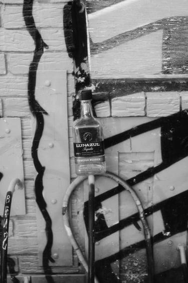 Black and white urban street art scene featuring a Lunazul Tequila bottle against a graffiti brick wall.