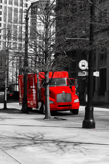 A vibrant red truck parked on a black and white city street with urban skyscrapers and bare trees.